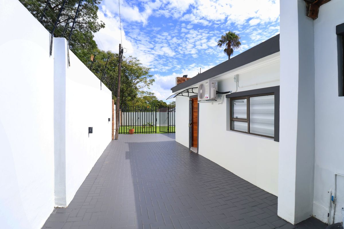 A well-maintained rear exterior area featuring a paved driveway, secure boundary wall with electric fencing, and an external air conditioning unit.