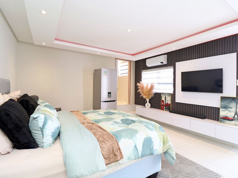 Modern bedroom featuring a slatted feature wall, built-in media console, recessed ceiling lighting with cove accents, and tiled flooring.