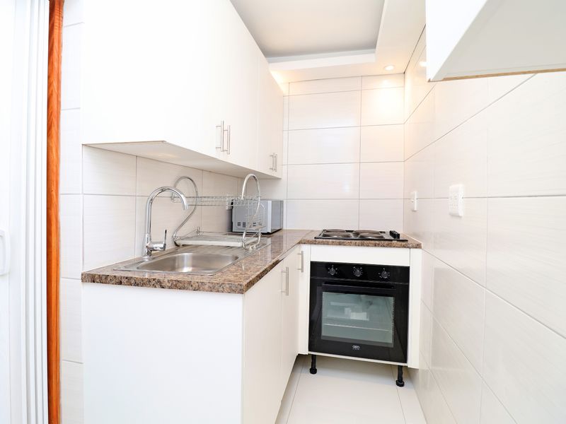 Compact modern kitchen featuring white cabinetry, granite countertops, stainless steel sink, and integrated oven with electric hob, finished with clean wall tiling.