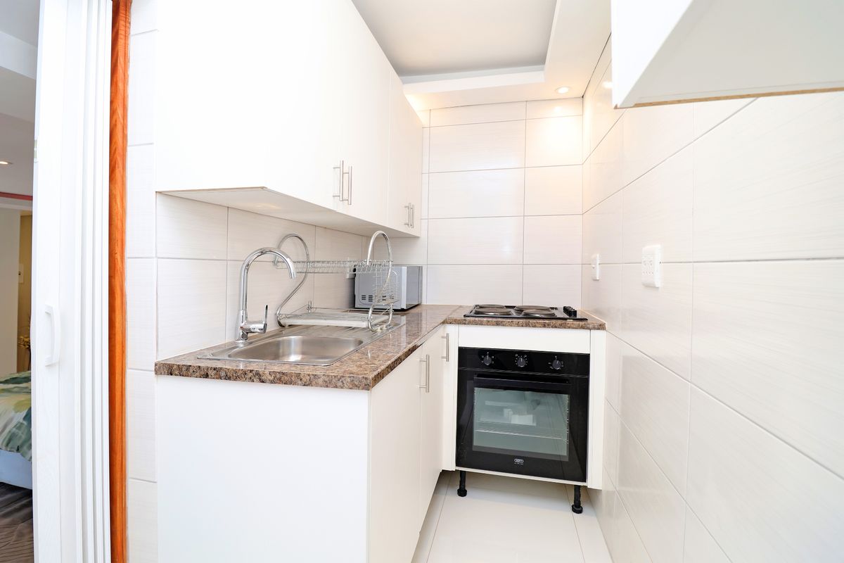 Compact modern kitchen featuring white cabinetry, granite countertops, stainless steel sink, and integrated oven with electric hob, finished with clean wall tiling.