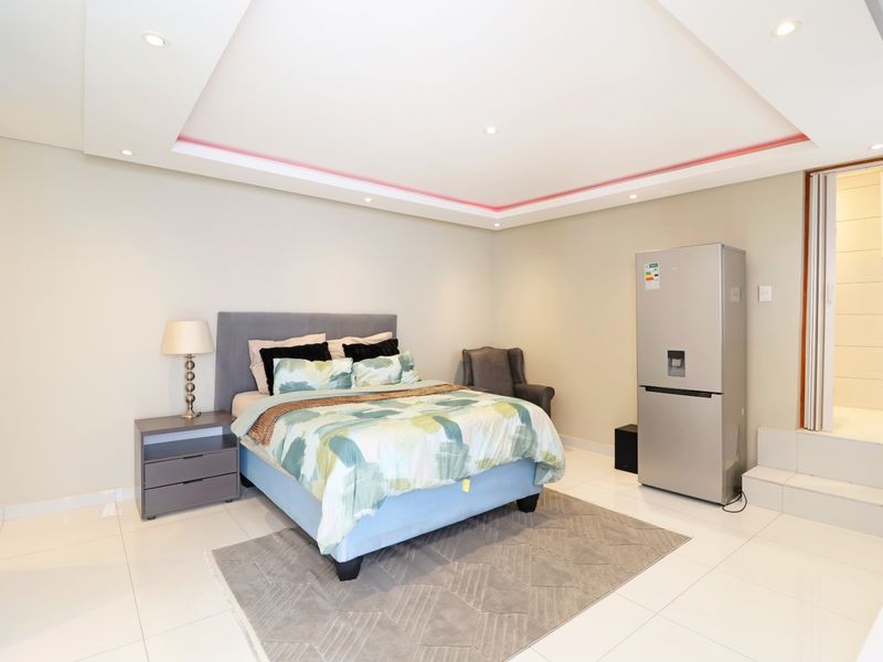 Spacious bedroom featuring a raised platform area, modern recessed ceiling with integrated LED lighting, and polished tiled flooring.