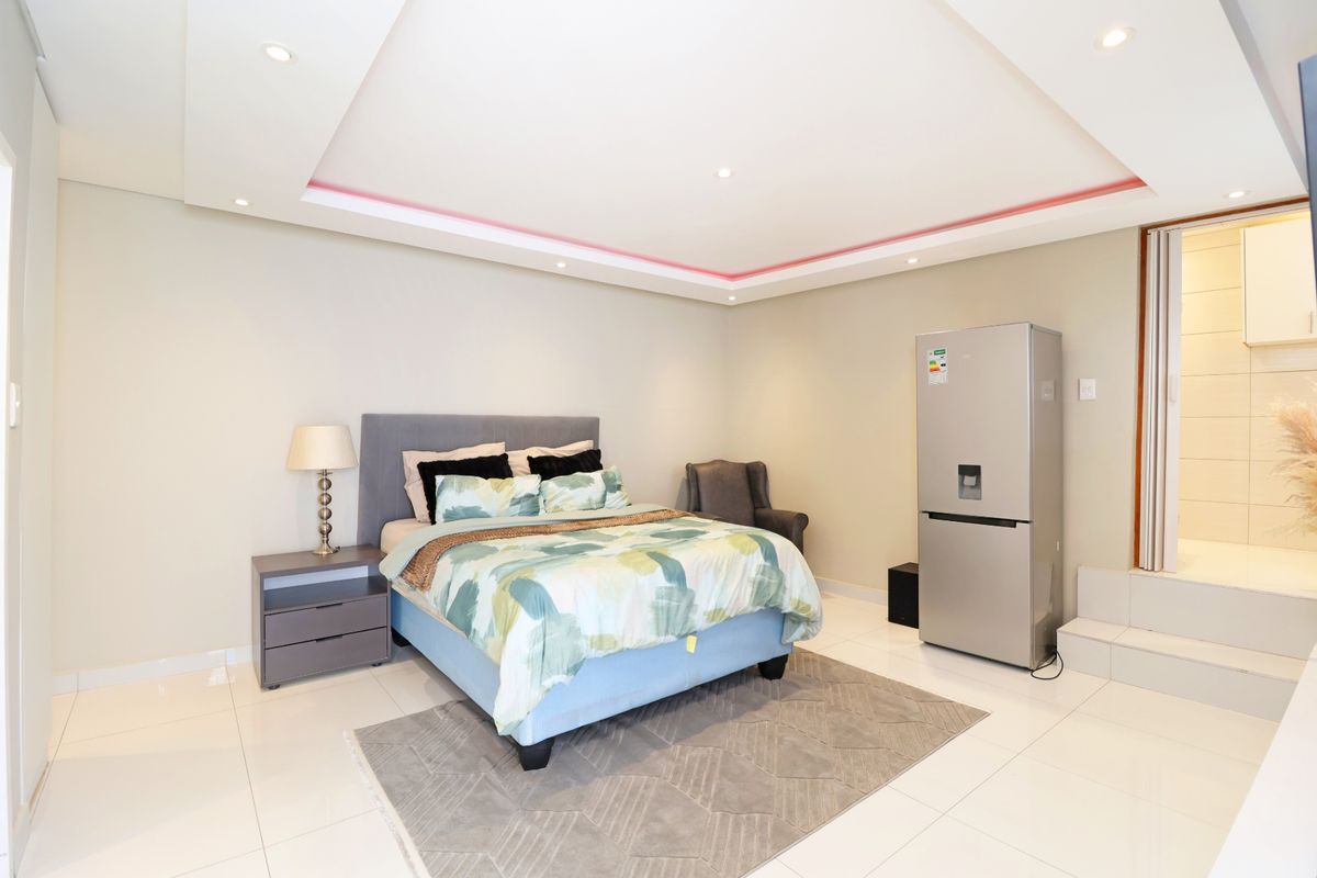 Spacious bedroom featuring a raised platform area, modern recessed ceiling with integrated LED lighting, and polished tiled flooring.