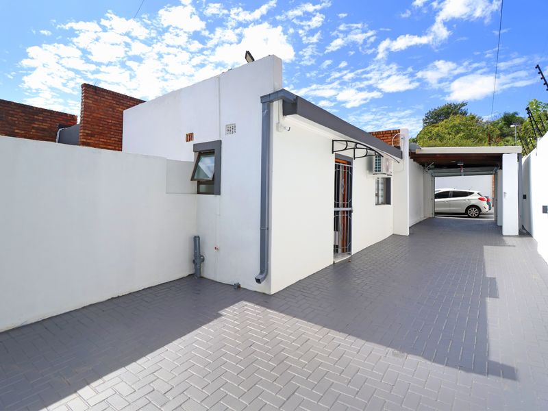 Exterior view of the apartment entrance featuring a paved driveway, secure gated access, and an installed air conditioning unit.