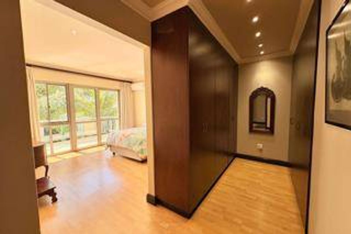 Spacious bedroom featuring extensive built-in cupboards, warm laminate flooring, recessed lighting, and a sliding glass door leading to an outdoor area.