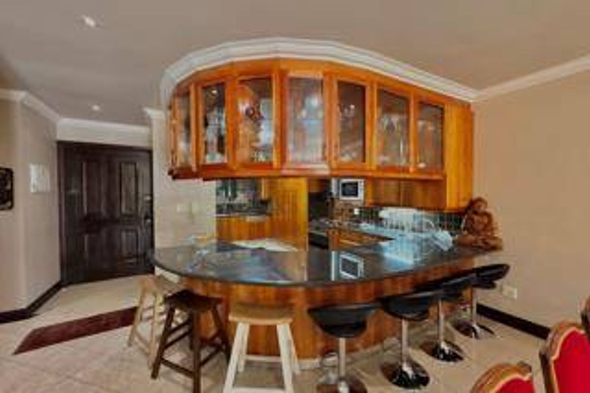 A kitchen featuring curved wooden cabinetry, glass-fronted display units, and a granite breakfast bar with integrated lighting and built-in microwave.