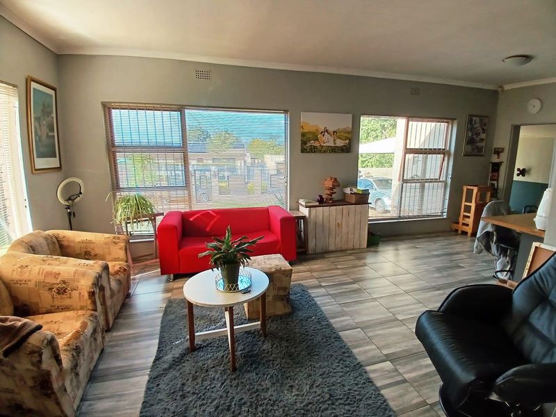 A spacious living room featuring large windows with venetian blinds, tiled flooring, and neutral wall tones, offering a bright and functional living space.