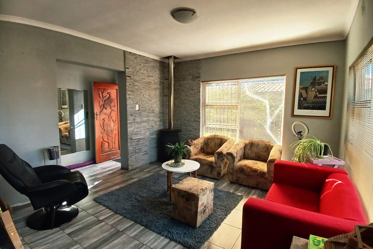 A comfortable living room featuring a stone-clad feature wall with a freestanding fireplace, tiled flooring, and natural light through venetian blinds.