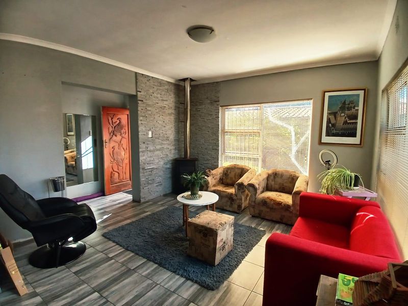 A comfortable living room featuring a stone-clad feature wall with a freestanding fireplace, tiled flooring, and natural light through venetian blinds.