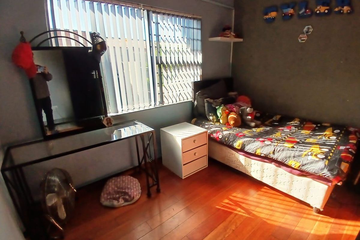 A bedroom featuring laminate flooring, vertical blinds with security gates, and a wall-mounted air conditioning unit.