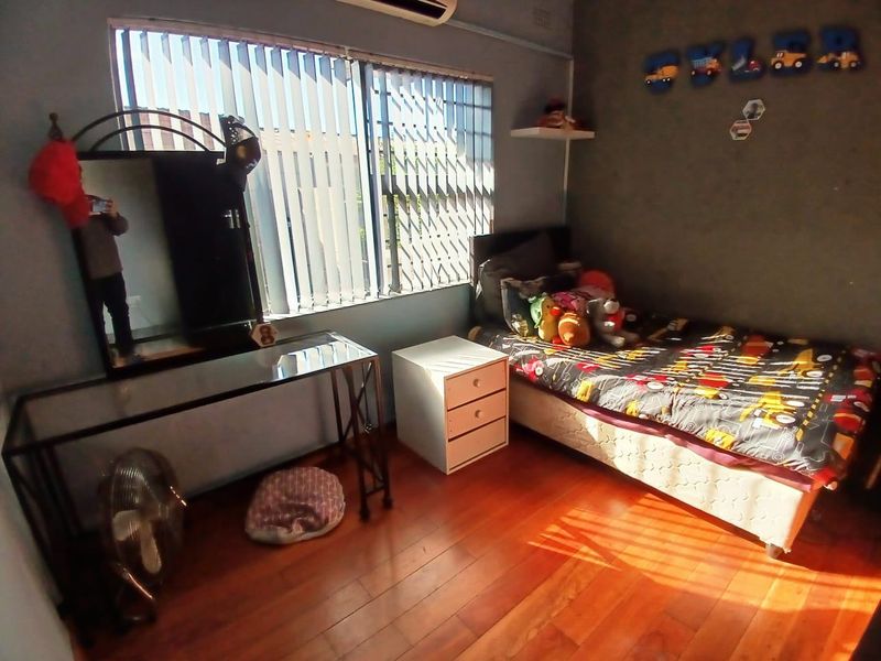 A bedroom featuring laminate flooring, vertical blinds with security gates, and a wall-mounted air conditioning unit.