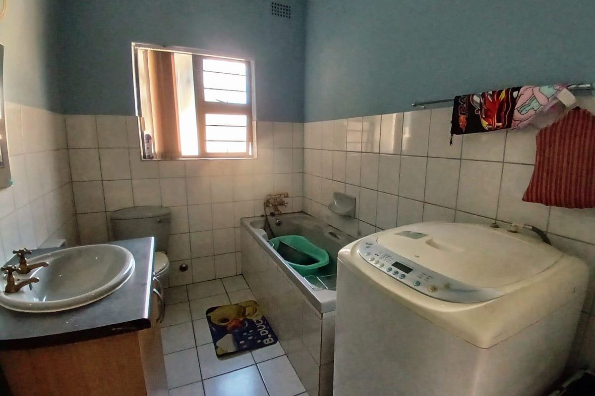 A functional bathroom featuring a built-in bathtub, vanity basin, and toilet, finished with tiled walls and flooring.