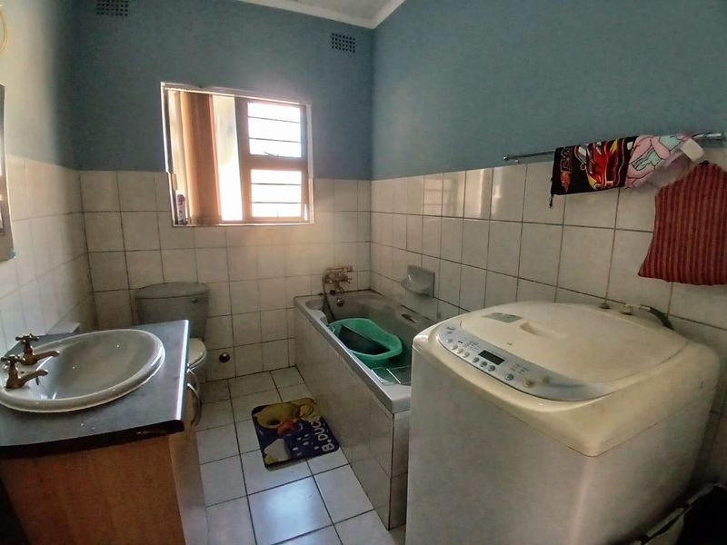 A functional bathroom featuring a built-in bathtub, vanity basin, and toilet, finished with tiled walls and flooring.