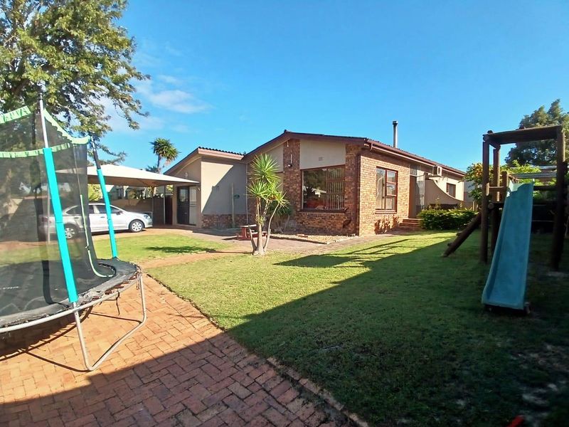 Rear view of a brick house featuring a paved patio area, a carport, and a spacious garden.