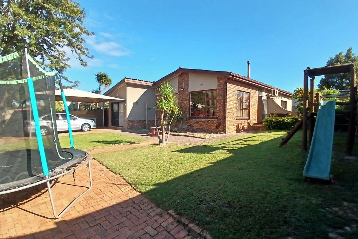 Rear view of a brick house featuring a paved patio area, a carport, and a spacious garden.