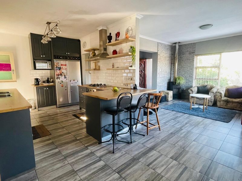 Open-plan living area featuring a modern kitchen with dark cabinetry, subway tile backsplash, kitchen island, and a cozy lounge area with a stone fireplace.