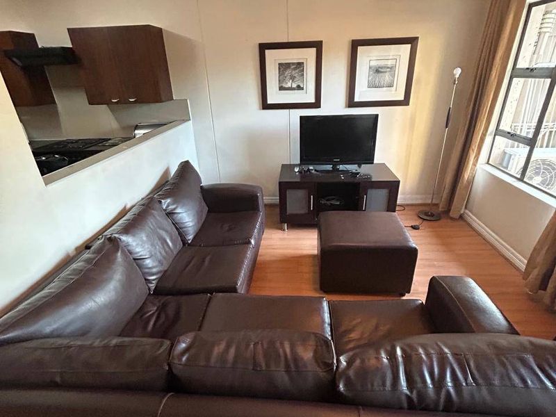 Open-plan living area featuring laminate flooring, a wall-mounted air conditioner, and an adjacent kitchen space with built-in cabinetry.