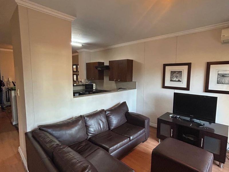 Open-plan living area featuring laminate flooring, coving, and a semi-open kitchen with built-in cabinetry and an extractor fan.