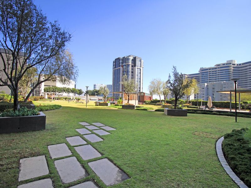 A well-maintained communal garden area featuring manicured lawns, stone paver pathways, and raised planters within an apartment complex setting.