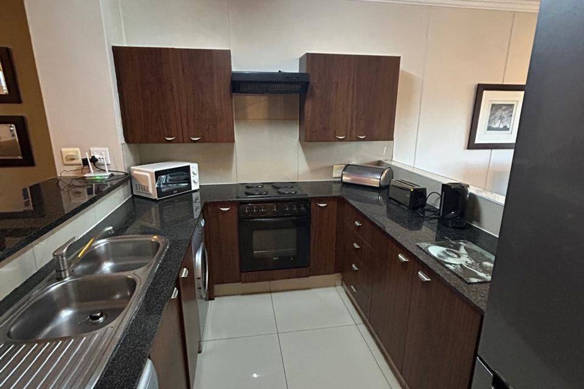 A functional kitchen featuring dark wood cabinetry, granite countertops, a built-in oven with hob, and tiled flooring in an apartment setting.