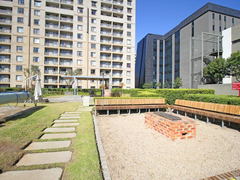 Communal outdoor area featuring a swimming pool, a built-in brick fire pit with integrated timber bench seating, and landscaped garden surrounds.