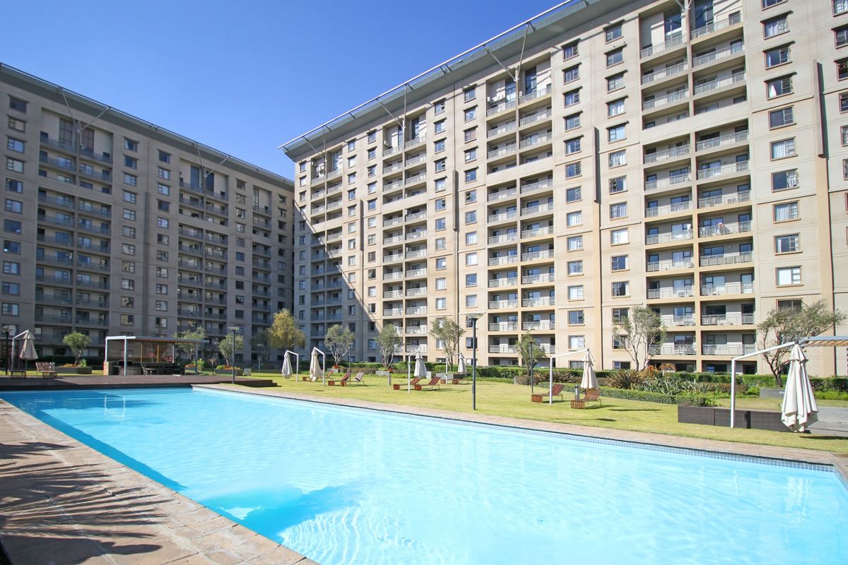 A well-maintained communal swimming pool area set within a landscaped garden, surrounded by large apartment buildings.