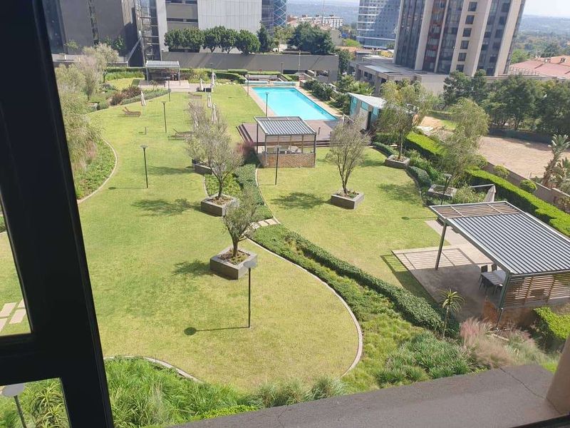 Elevated view overlooking a well-maintained communal garden area featuring a swimming pool, landscaped lawns, and covered outdoor entertainment structures.