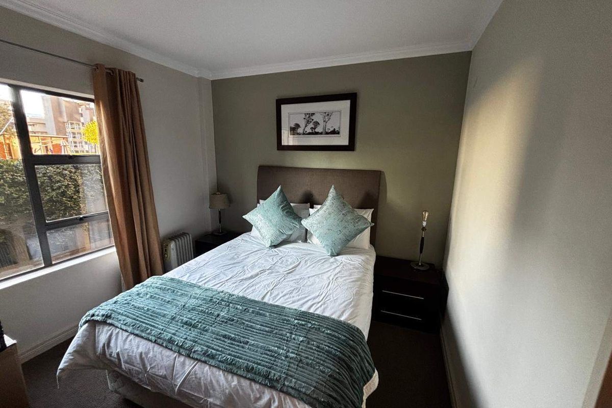 A cozy bedroom featuring carpeted flooring, neutral wall tones, and an aluminium-framed window providing natural light.
