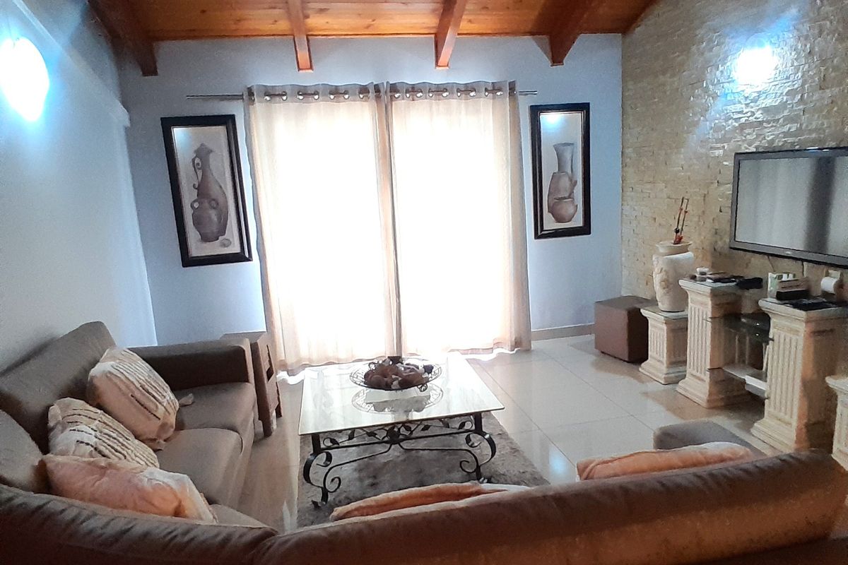 A cozy living room featuring a striking stone accent wall, exposed timber ceiling beams, and neutral tiled flooring, creating a warm and inviting atmosphere.