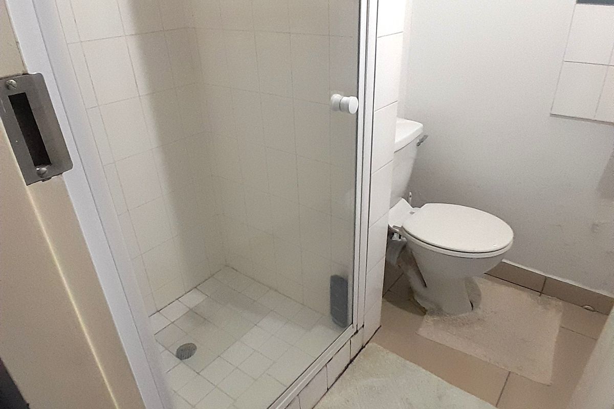 A compact bathroom featuring a tiled shower enclosure and a standard toilet, requiring some cosmetic updates to improve its overall condition.
