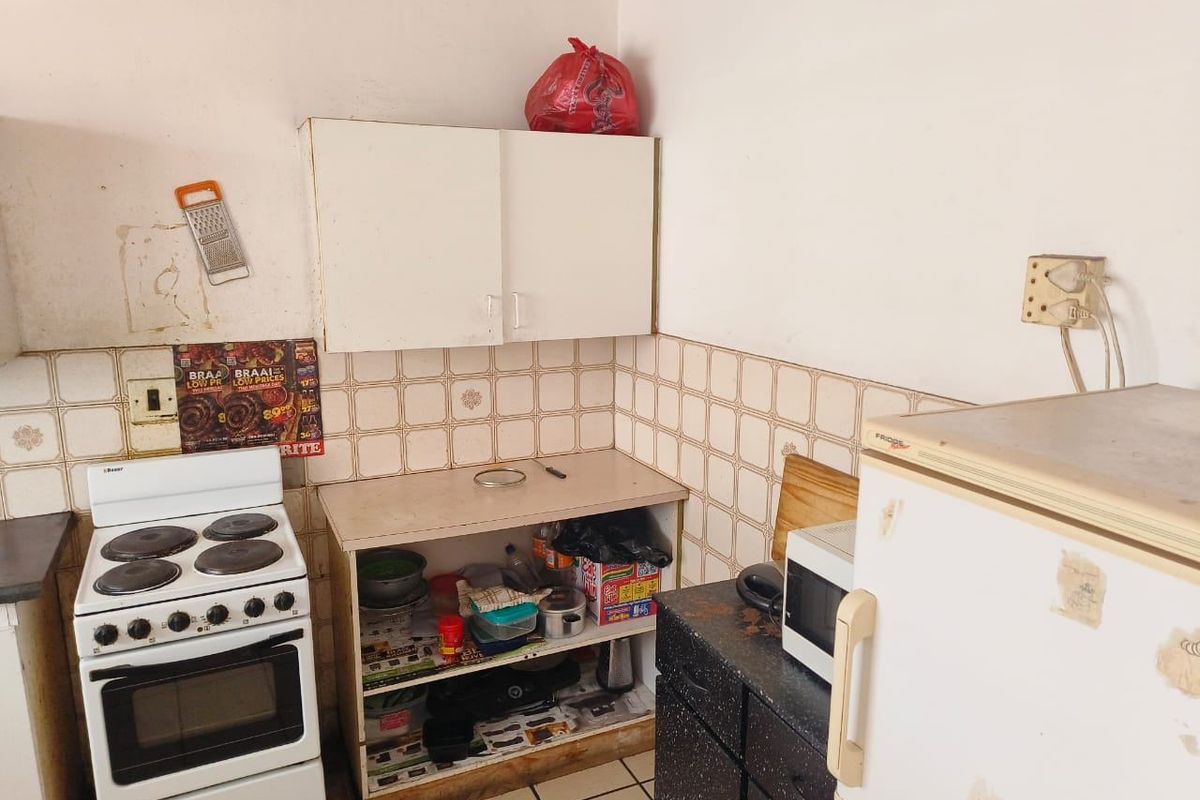 A compact kitchen area featuring a built-in stove, tiled backsplash, and wall-mounted cabinetry, requiring cosmetic updates and maintenance to improve its overall condition.