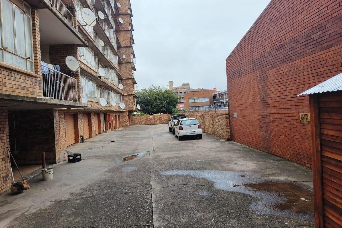 Rear exterior view of an apartment building showing a concrete parking area, brick facade, and multiple balconies with satellite dishes.