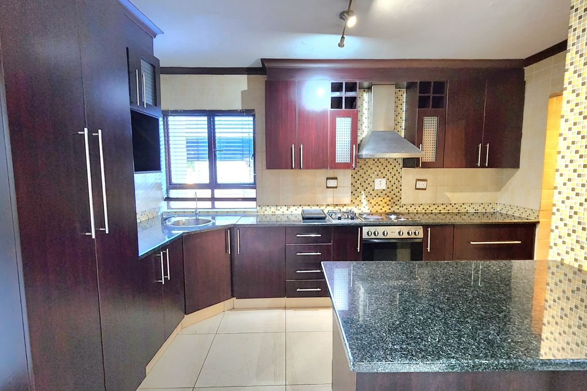 Modern kitchen featuring dark wood cabinetry, granite countertops, mosaic tile backsplash, and integrated stainless steel appliances including an oven and gas hob.