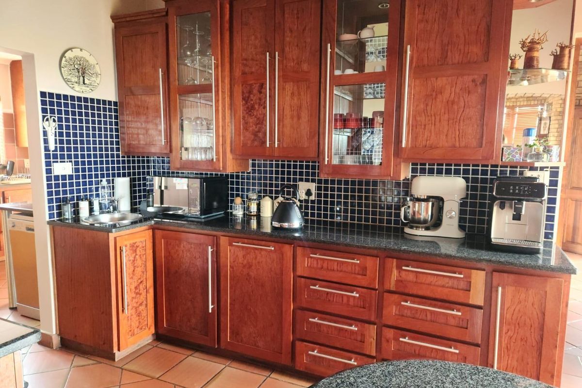 A functional kitchen featuring warm-toned wooden cabinetry, dark granite countertops, and a blue mosaic tile backsplash with terracotta floor tiles.