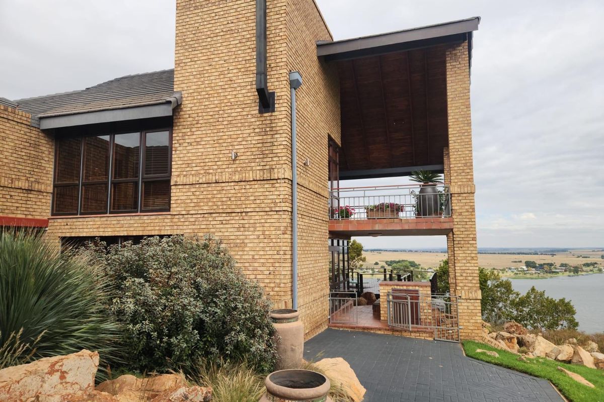 Rear elevation of a multi-level face brick home featuring a covered balcony, paved patio area, and expansive views of the surrounding landscape and water.
