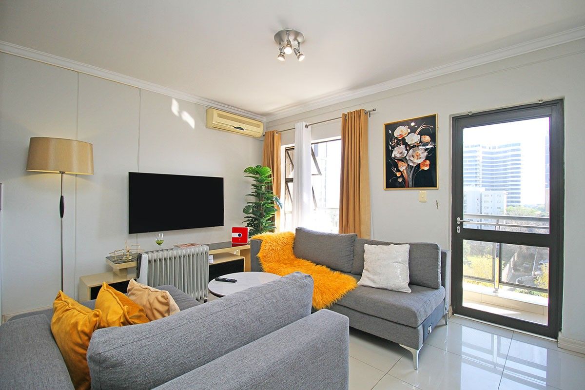 A well-lit living room featuring tiled flooring, a wall-mounted air conditioning unit, and direct access to an outdoor balcony area.