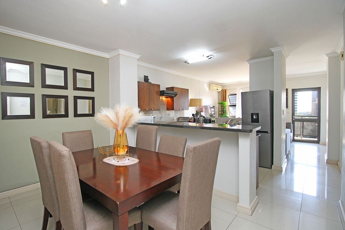 Open-plan dining and kitchen area featuring tiled flooring, granite countertops, and built-in cabinetry, leading to a balcony with natural light.