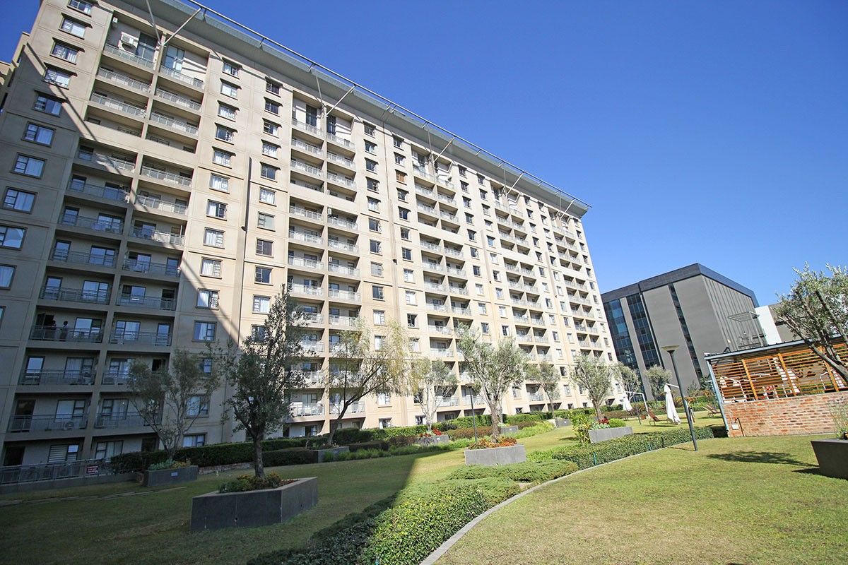 A view of the rear facade of a large apartment complex featuring multiple balconies and a well-maintained landscaped garden area.