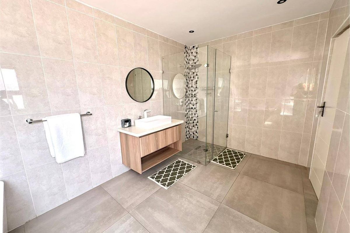 Modern bathroom featuring a floating vanity with a vessel sink, a spacious walk-in shower with glass enclosure, and neutral floor-to-ceiling tiling.