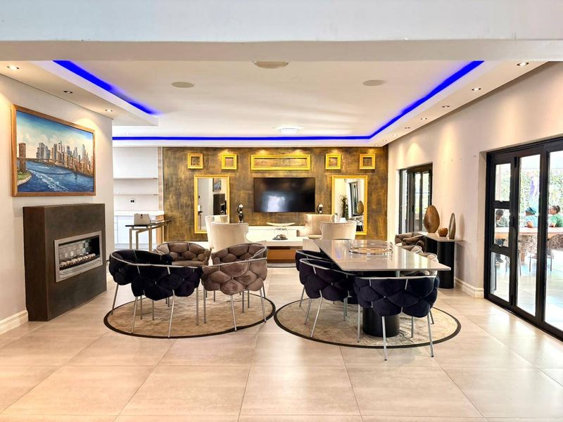 Spacious open-plan living and dining area featuring modern recessed ceiling lighting, LED accents, tiled floors, and a built-in fireplace with direct patio access.