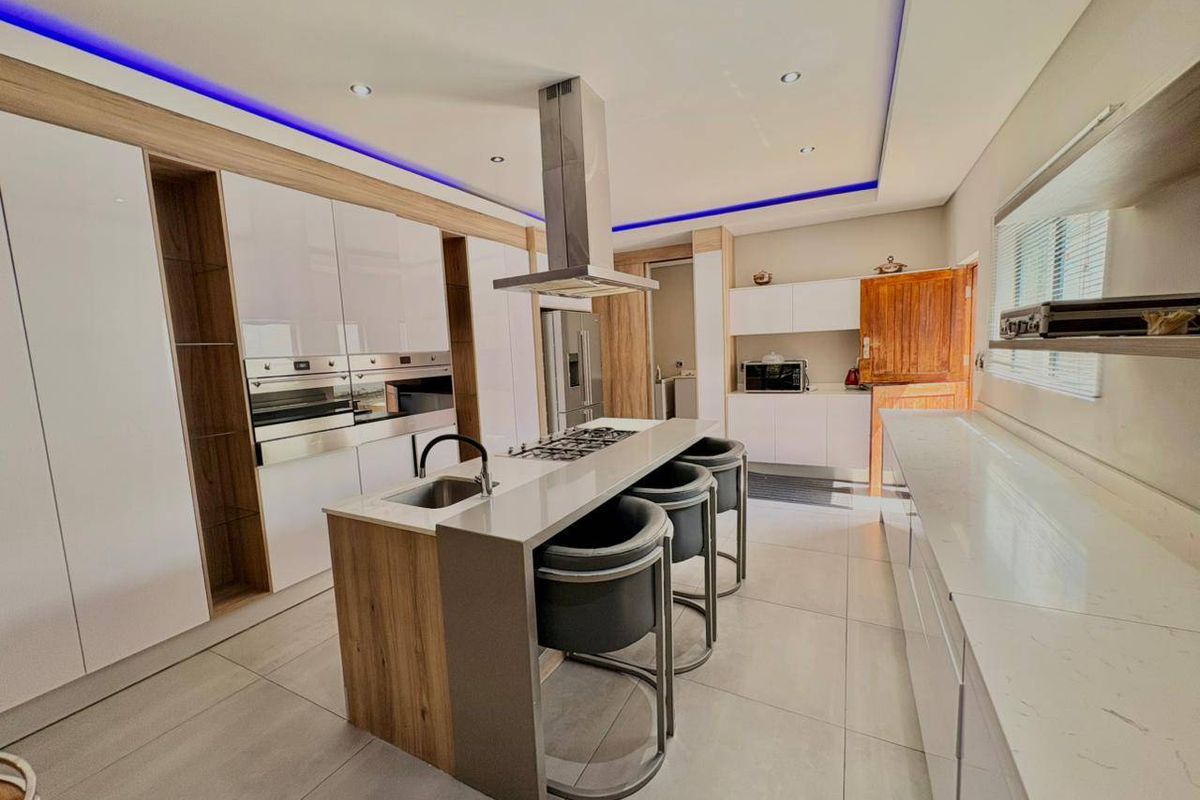 Modern kitchen featuring a central island with gas hob, integrated appliances, sleek cabinetry, quartz countertops, and ambient LED ceiling lighting.