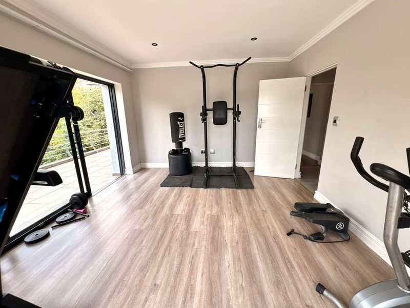 A well-maintained home gym featuring laminate flooring, recessed lighting, and a sliding glass door providing access to an outdoor balcony area.