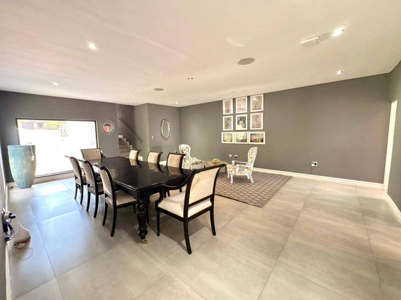 Spacious dining area featuring large format floor tiles, recessed ceiling lighting, and an open-plan layout with an adjacent staircase.