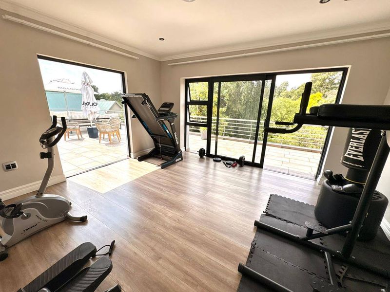 A bright home gym featuring laminate flooring, recessed lighting, and large sliding glass doors providing access to an outdoor balcony area.