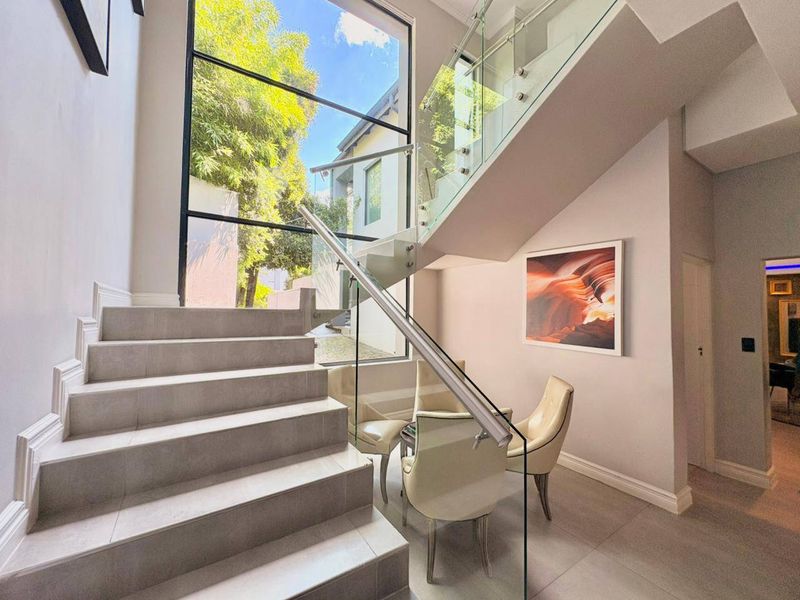 Modern entrance hall featuring a tiled staircase with a sleek glass balustrade and a large window providing ample natural light.