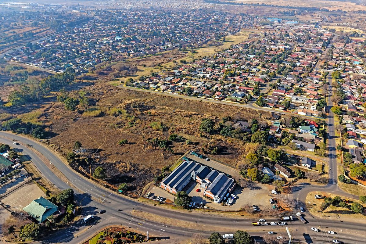 An aerial view of a large vacant residential development site situated near existing suburban housing and main road infrastructure.