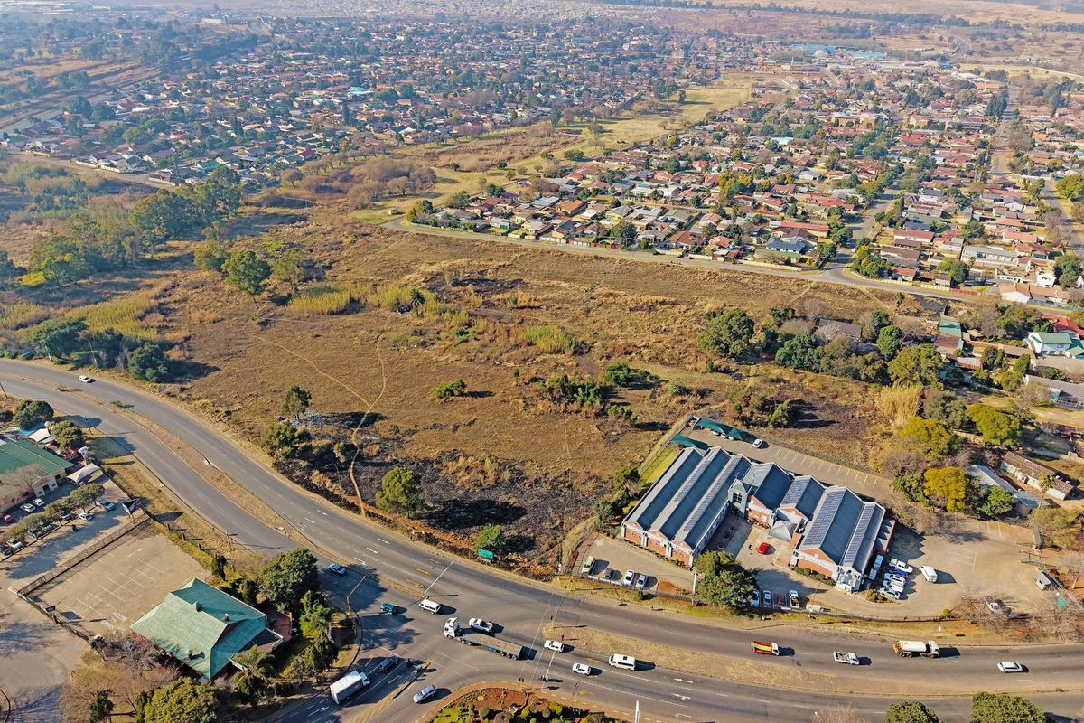 Aerial view of a large vacant residential land parcel situated near a main road and existing commercial infrastructure.