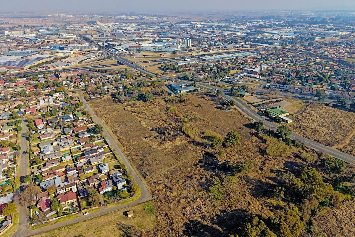 An aerial view of a large vacant residential plot situated within an established suburban area with nearby road access and industrial infrastructure.