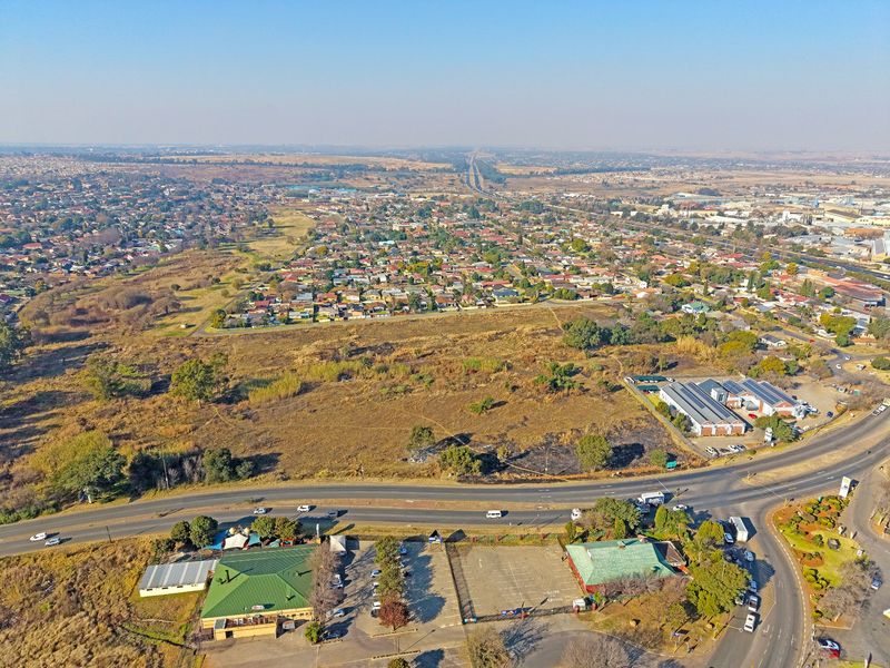 Aerial view of a vacant residential land plot situated near established commercial infrastructure and residential neighborhoods.
