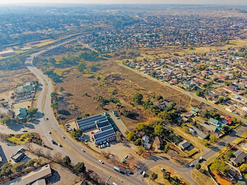 An aerial view showing a large tract of undeveloped residential land situated adjacent to established suburban housing and commercial infrastructure.