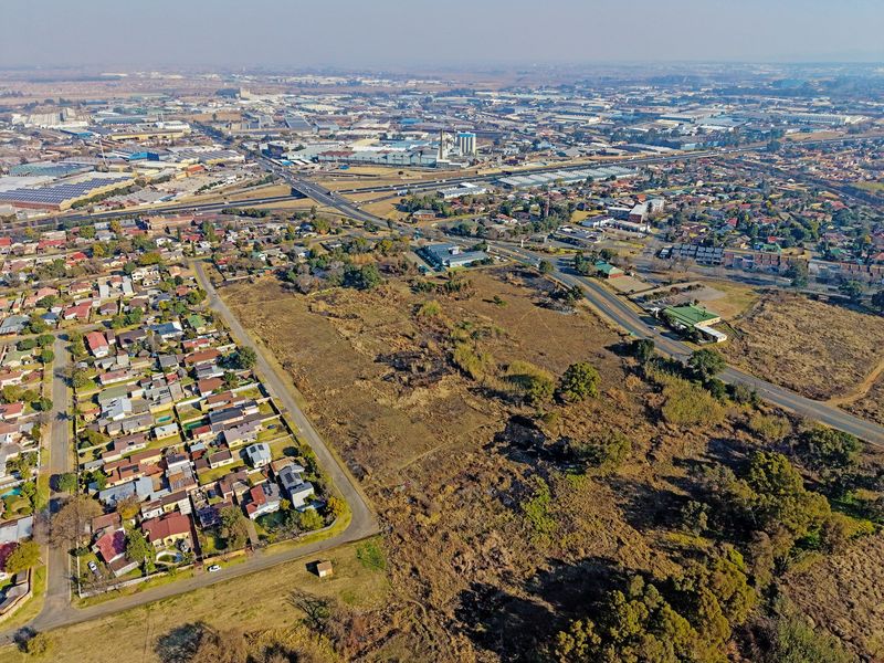 An aerial view of a large vacant residential plot situated within an established suburban area with nearby road access and industrial infrastructure.